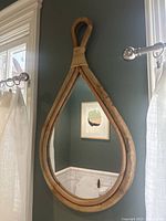 Vintage teardrop-shaped mirror with a natural wood frame and looped hanging top, mounted on a dark wall near a window.