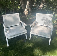 Two white outdoor cane-back chairs with cushions shown from front-side angle on grass