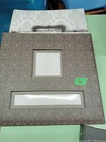 Two photo albums stacked, front album with patterned brownish-grey cover with window cutouts, back album white with floral pattern.