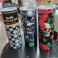 Photo of three travel cups with individual graphic designs placed on a black surface.