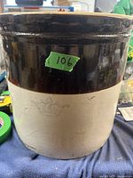 Photo showing front of crock with dark brown glaze upper half and beige lower half. Crown emblem visible on front.