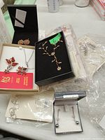 Lot of assorted new costume jewelry including gold-tone floral necklace with matching earrings, pearl drop earrings, silver hoops, leaf-shaped brooch, and linked chain bracelets