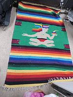 Full view of Mexican woven blanket laid flat showing colorful horizontal stripes and central figure in headdress.