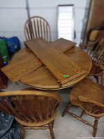 Round oak dining table with two leaf extensions on top and four surrounding chairs.