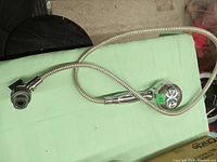 Photo of a chrome finished shower head attached to a flexible metal hose laid out on a green surface showing connectors and spray face.