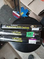 Photo showing three VHS tapes of Tim Burton's The Nightmare Before Christmas stacked on a round black table with some boxes, broom, and dustpan in the background.