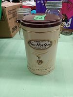 Photo of a cream-colored metal Tim Hortons coffee tin with maroon lid and latch, showing brand logo and coffee-related graphics.