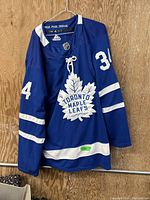 Front view of blue Adidas Toronto Maple Leafs hockey jersey with white stripes, team crest and number 34 on sleeves