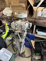 Full view of vintage Johnson outboard motor showing metal body, attached cables, and propeller, placed in a workshop environment with boxes and other items around.