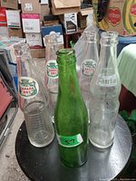 Photo showing five vintage pop bottles placed together on and around a chair, including three Canada Dry bottles, one Fanta bottle, and one green unbranded bottle.