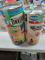 Two vintage Tinkertoy construction sets in original cylindrical containers with green tape seals.