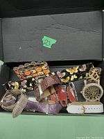 Photo showing the full lot of assorted watches and bracelets inside a black box, including various watch bands and decorative wide cuff bracelets.