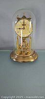 Full view of the anniversary clock under a glass cloche dome showing the entire clock and base.