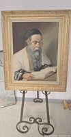 Frontal view of the oil painting showing the full framed image of a Rabbi reading a book placed on a stand.