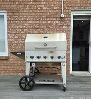 Full view of stainless steel gas grill on deck with brick background
