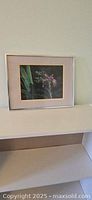 Framed iris flower painting with beige matting and silver frame, seen hanging on wall.