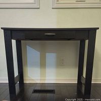 Front view of black composite wood desk showing drawer and legs.
