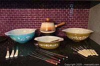 Full lot overview showing two Pyrex bowls (blue with Hot Air Balloon pattern, olive with Crazy Daisy pattern), enamelled fondue pot, several knives and fondue forks.