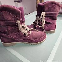 Side angle view showing purple suede boots with beige striped laces and padded fleece lining visible at collar, set against a glass surface.