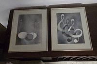 Two framed monochromatic art pieces side-by-side on a wooden surface showing abstract musical note designs.