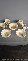 Full set includes three Royal Doulton Bunnykins cups and three matching bowls, all decorated with child-friendly bunny illustrations and cream background, plus one small Beatrix Potter mug with story text and character images.
