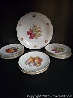 Set of 11 smaller fruit plates and 1 large platter displayed together, showing scalloped edges and gold trim with various fruit designs.