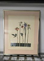 Full view of the framed art print showing six stylized flower stems, the silver metal frame, and pale pink mat.