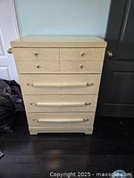 Full front view showing the tall boy dresser with four drawers and gold-tone metal knobs and bar handles.