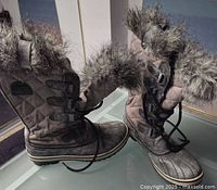 Full side and front view of the pair of women's winter boots. Showcases faux fur cuff, quilted waxed canvas upper in distressed gray with leather overlays, lace-up front.