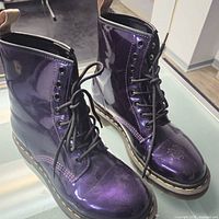 Front angle view of pair of purple patent leather 8-hole lace-up Dr. Martens boots with black laces and yellow sole stitches.