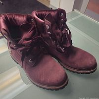 Pair of women's purple suede Timberland workboots on glass table, angle showing front and top of boots with laces untied.