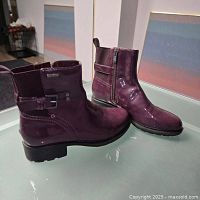 Photo of both purple Rockport ankle boots, showing the side profile with strap and zipper detail and shiny patent finish.