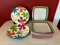 View of the 16 plates stacked and displayed, showing both square striped plates and round floral plates.
