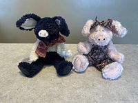 Front view of both plush pig collectibles, one dark blue and white with bow and one pink in floral outfit.