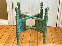 Front view of antique green folding planter stand showing carved decorative panels and turned legs with square finials.