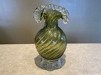 Front view of avocado green ribbed glass vase with clear ruffled rim and base on neutral surface.