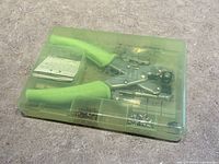 Closed plastic case containing Crop-A-Dile hole punch tool with green handles and assorted accessories visible inside.