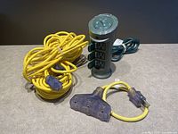 Photo showing the yellow extension cord, yellow 3-outlet adapter, and black outdoor timer arranged together on a surface.
