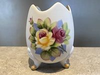 Front view of the cracked egg shaped hand painted vase showing detailed floral design and gold tipped legs.