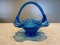 Front view of aqua blue glass basket dish with handle on pedestal base and wavy rim.