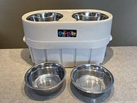 Front view of adjustable white pet feeder with 4 stainless steel bowls (2 in feeder, 2 in front).