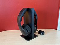 Side view of Sony wireless headphones placed on the black transmitter stand with AC adapter beside it on table.