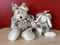 Two vintage Boyds Bears plush toys, Ophelia the White Bear and Julip O'Harea the White Rabbit, posed together on a wooden surface with red wall background, both wearing matching floral outfits with tags.