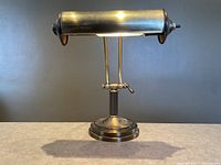 Front view of vintage brass bankers lamp showing cylindrical shade and round base with adjustment mechanism.