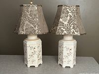 Pair of vintage Japanese ceramic lamps on a surface with decorative floral motifs and fabric shades, photographed in daylight.