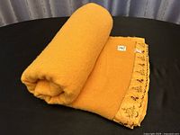 Rolled up orange wool blanket on black surface.