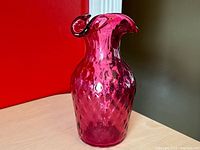 Full view of the cranberry colored glass vase showing the textured pattern and curled ruffled lip