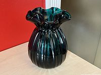 Front angle close-up showing the blue green teal glass vase with vertical ribbed design and ruffled rim.
