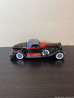 Side view of the Avon Auburn 1932 car bottle showing black and orange body with gray roof and white wheels.