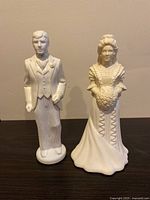 Front view of Avon bride and groom porcelain figurines placed on a dark surface against a beige wall.